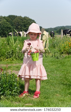 A girl in a field holds a bucket of flowers.