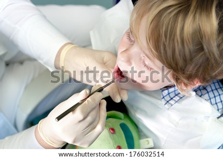 A gloved dentist inserts a dental tool into a boy\'s mouth.