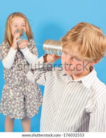 A girl talking into a tin can tied to a string while a boy listens.