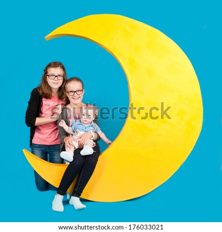 Two young girls smiling holding a toddler while sitting on a half moon.