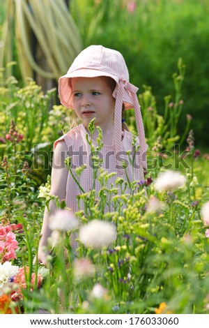 A girl wearing a floppy hat in a field of wild flowers.