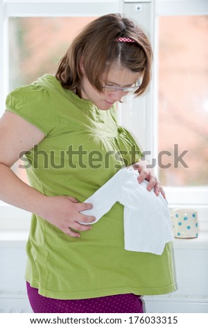A pregnant woman looking at a baby white shirt on her belly.