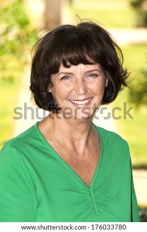 A lady wearing a green shirt smiling on a sunny day.