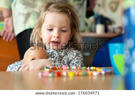 A little girl holding a doll at a table with a candy necklace on it.