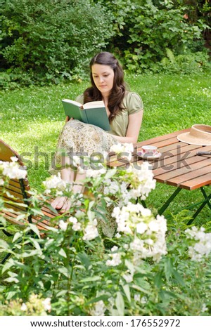 A woman reads a book while she sits at a table outside.