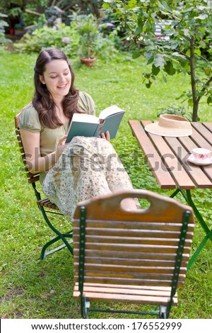 A woman sitting with her feet up on a chair reading a book.