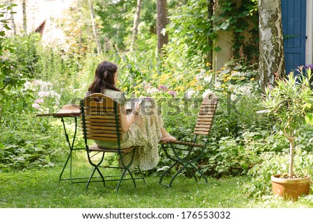 A woman sits on a chair in a garden.