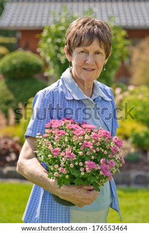 A lady in a blue plaid shirt holding a pot of pink flowers.