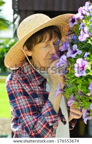 Older lady in straw hat smelling purple flowers.