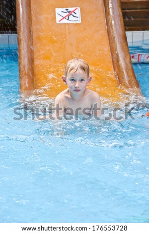 A boy in a swimming pool next to an orange slide with a no running sign.