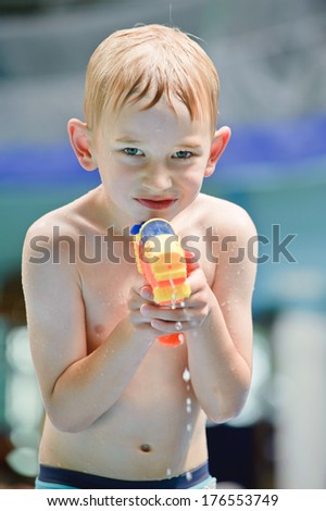 A young boy with no shirt squirting a water gun.