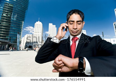 A man in a suit holds a phone while looking at his watch.