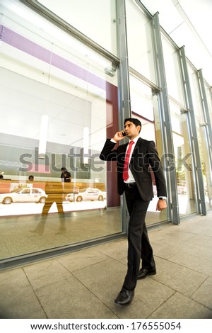 A man in a suit is using his cell phone whilst walking past a large window.