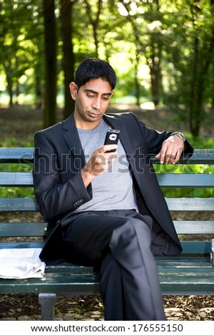 A man sitting on a park bench while looking at his cell phone.