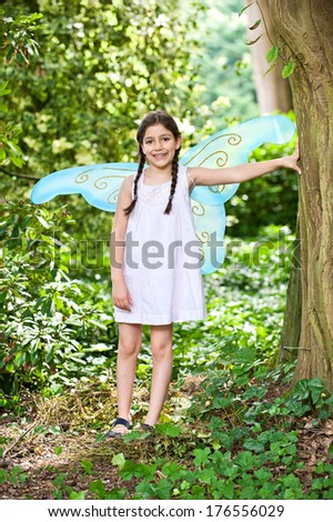 A young girl with fairy wings standing in a garden.