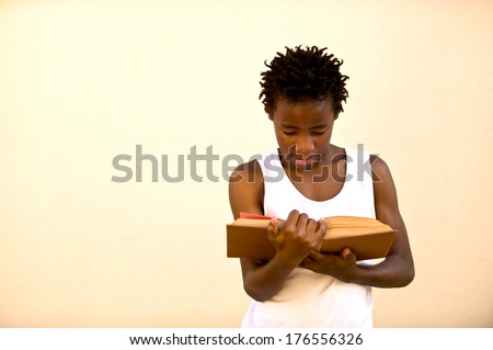 A young African man wearing a white vest reading a book.