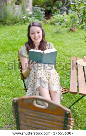 A woman sitting outside holding a book while smiling.