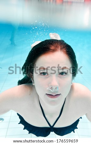 A girl in a blue bathing suit swimming under water with her eyes open.
