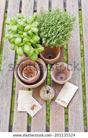 a choice of potts and herbs on a table with seeds in paper bags, cord and scissors