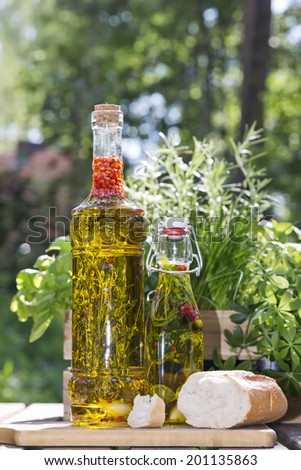 herbs in a bottle with olive oil standing next to fresh bread on a cutting board in the garden