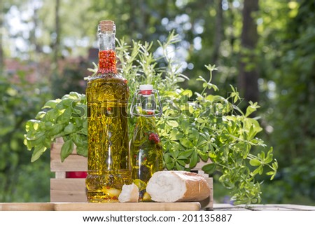 herbs in a bottle with olive oil standing next to fresh bread on a cutting board in the garden