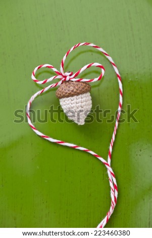 a partly crochet acorn on green background with a red and white thread shaping a heart