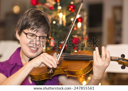a woman playing the violin in front of a christmas tree at home