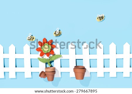 crochet flower with pots, bees and a white fence on blue background