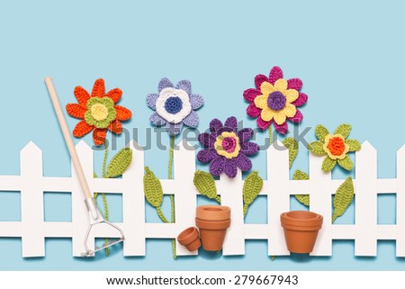 crochet flowers behind a white paper fence with flower pots and a rake on blue background