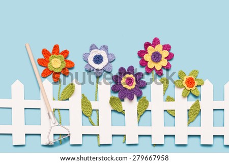 crochet flowers behind a white paper fence with a rake on blue background