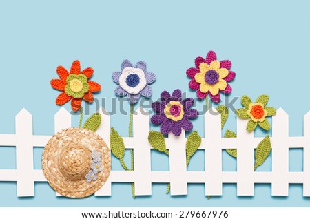 crochet flowers behind a white paper fence with a hat on blue background