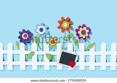 crochet flowers behind a white paper fence with a tag and a red heart on blue background