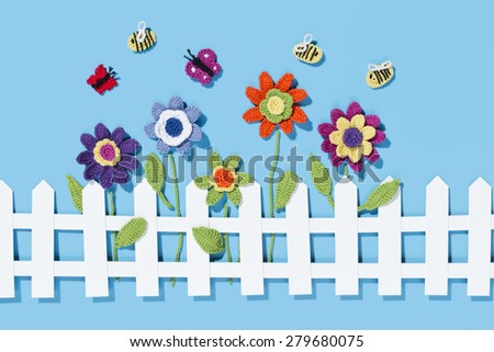 crochet flowers behind a white paper fence with bees and two butterflies on a blue background