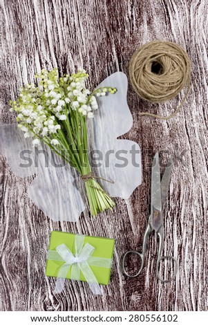 a bouquet of Lily of the Valley with a plastic butterfly, a present, scissors and a cord on a wood textured imitation