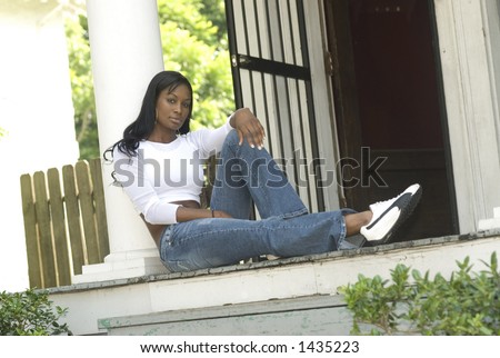 african american woman sitting on the porch of an older home - urban setting