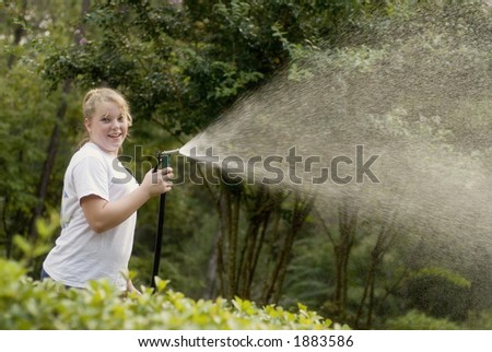 Young blond girl at home with a water hose spraying the plants