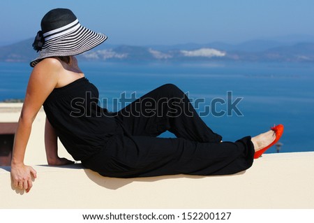 Beautiful woman in a straw hat on the villa's roof with view to Aegean sea