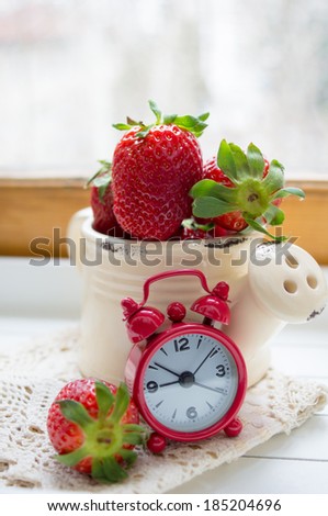 Fresh strawberries on the table and old-styled red clock