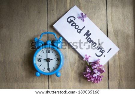 Good morning note, lilac flowers and old-styled clock on the wooden table