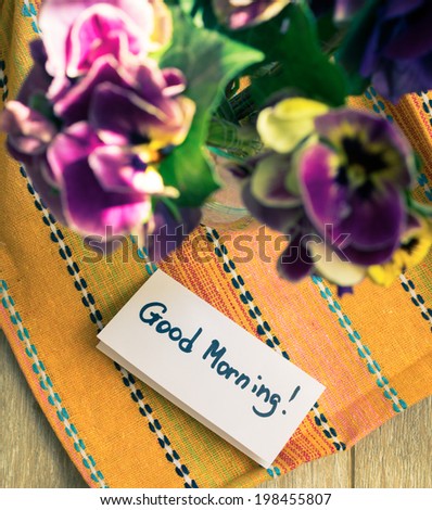 Viola flowers in a vase, old-styled clock and Good morning note on the table
