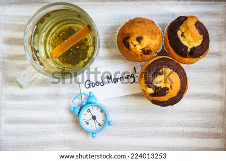 Cup of hot green tea, cupcakes and Good morning note on the wooden table