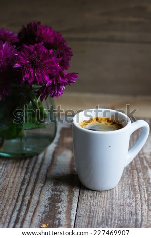 Cup of coffee, note and flowers on the old wooden table