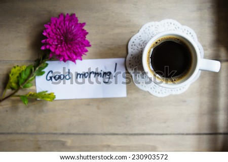 Cup of coffee, note and flowers on the old wooden table