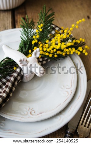 Spring festive dining table setting with yellow mimosa flowers, candles, napkins and vintage cutlery on a wooden board