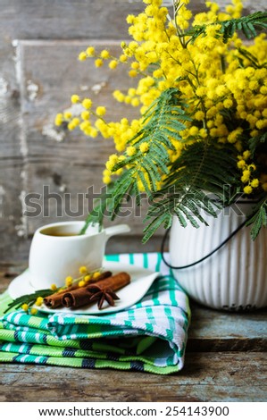 Glass cup with tea and blooming yellow mimosa with good morning note on wooden background