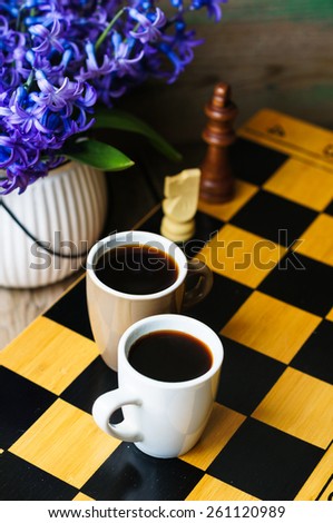 Cup of coffee on the chess board and first spring flowers Scylla