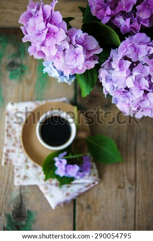 Hydrangea flowers in a vase and cup of coffee on the wooden table