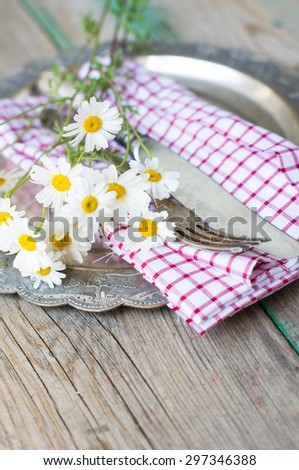 Summertime Table Setting with daisy flowers, napkin and silverware on wooden table