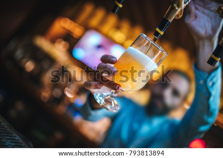 Barmen or brewer filling glass with beer. Barmen is pouring lager beer to glass from  beer taps. Bar or night club interior