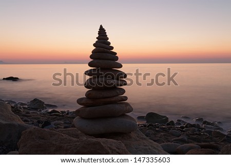 Stack of  balanced pebbles in front of view of sea at sunset.